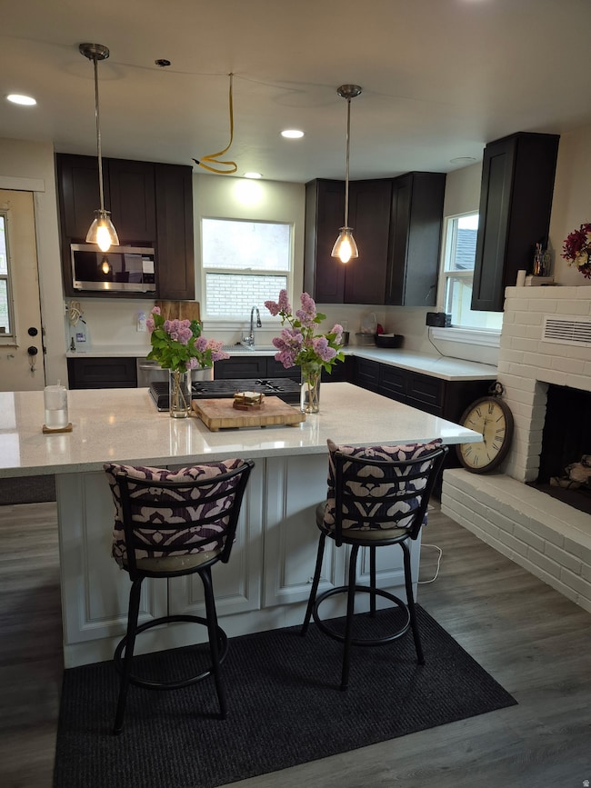 Kitchen with dark wood-style floors, a breakfast bar area, pendant lighting, stainless steel microwave, and recessed lighting