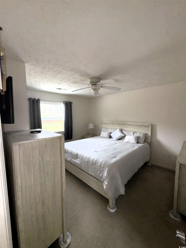Bedroom with a textured ceiling, dark colored carpet, and ceiling fan
