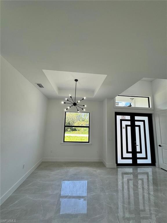 Unfurnished dining area featuring a raised ceiling, a chandelier, and light marble finish flooring