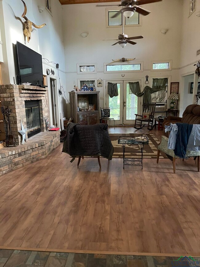 Living area with a towering ceiling, a ceiling fan, wood finished floors, and a fireplace