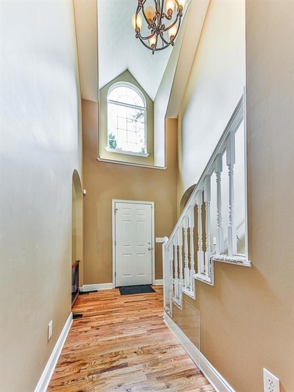 Entrance foyer featuring high vaulted ceiling, stairway, a chandelier, light wood-style flooring, and arched walkways