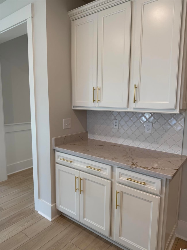 Kitchen with baseboards, white cabinetry, light st