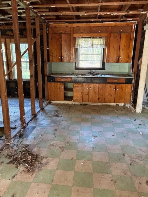 Kitchen with tile patterned floors, backsplash, brown cabinetry, and dark countertops