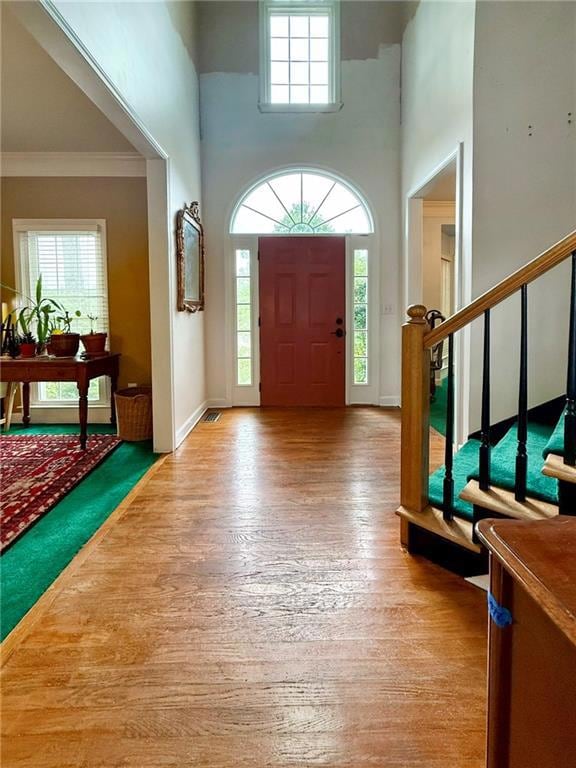 Entrance foyer with light wood-style flooring, plenty of natural light, a towering ceiling, stairs, and crown molding