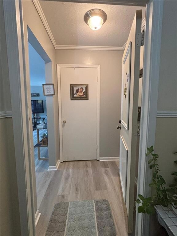 Hallway featuring wood finished floors, a textured ceiling, crown molding, and baseboards