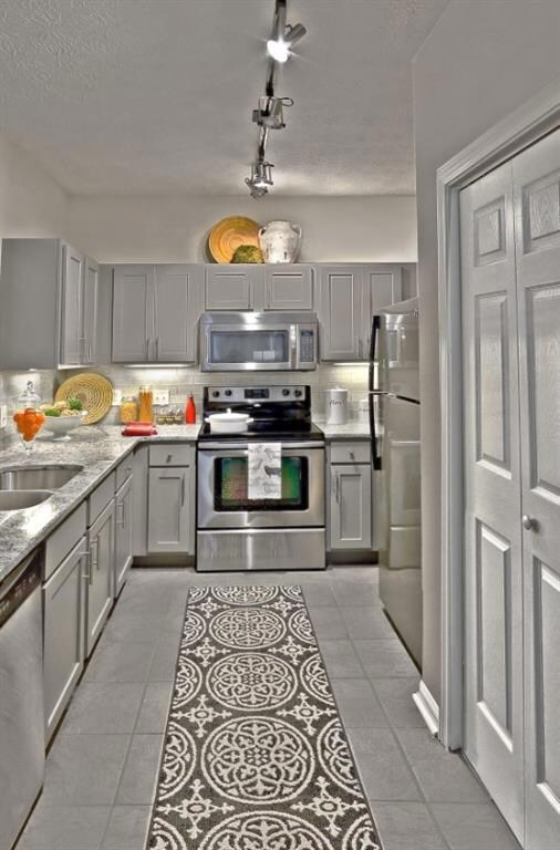 Kitchen featuring track lighting, decorative backsplash, appliances with stainless steel finishes, light tile patterned floors, and gray cabinetry
