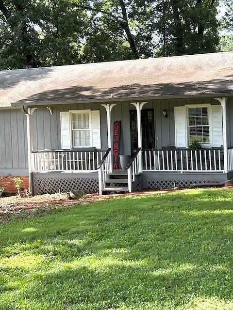 Ranch-style home featuring covered porch, a front lawn, and a shingled roof