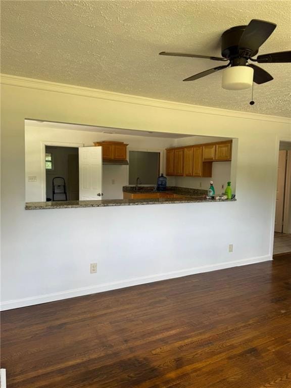 Kitchen with brown cabinets, dark wood-style floors, crown molding, a textured ceiling, and a ceiling fan