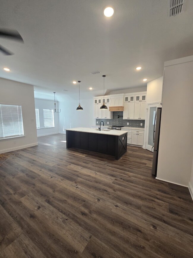Kitchen featuring glass insert cabinets, white cabinetry, pendant lighting, open floor plan, and a kitchen island with sink