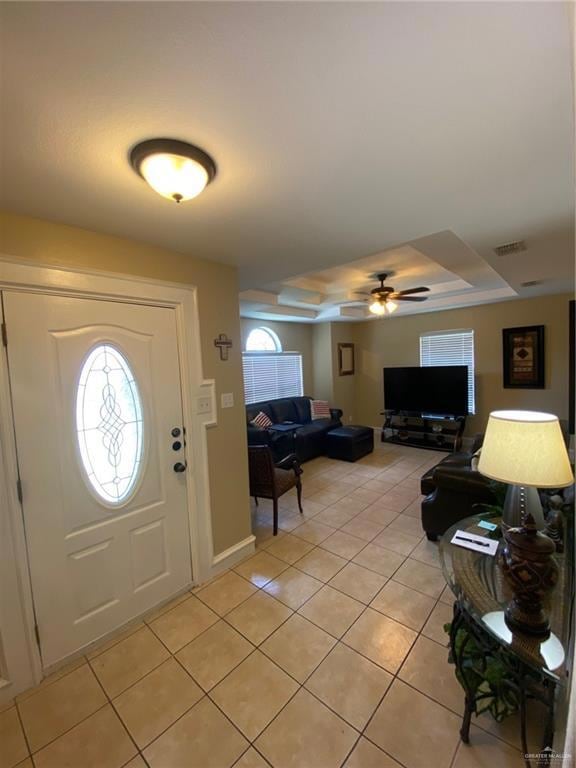 Foyer entrance with a raised ceiling, light tile patterned floors, and a ceiling fan