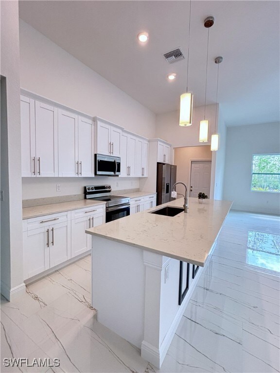 Kitchen with appliances with stainless steel finishes, a sink, light marble finish flooring, baseboards, and white cabinets