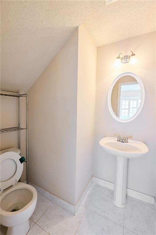 Bathroom with a textured ceiling, toilet, and base