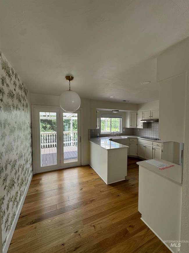 Kitchen with wallpapered walls, a peninsula, dark wood-style floors, white cabinets, and backsplash