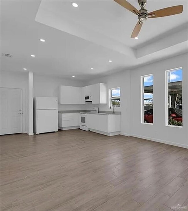 Unfurnished living room with a tray ceiling, recessed lighting, a ceiling fan, and light wood-style floors