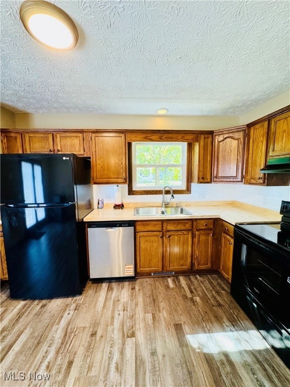 Kitchen featuring black appliances, brown cabinetry, light wood-type flooring, light countertops, and a textured ceiling