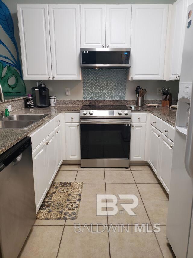 Kitchen with appliances with stainless steel finishes, white cabinetry, and light tile patterned floors