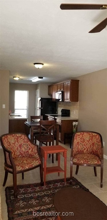 Kitchen featuring light tile patterned floors, light countertops, black appliances, and a ceiling fan