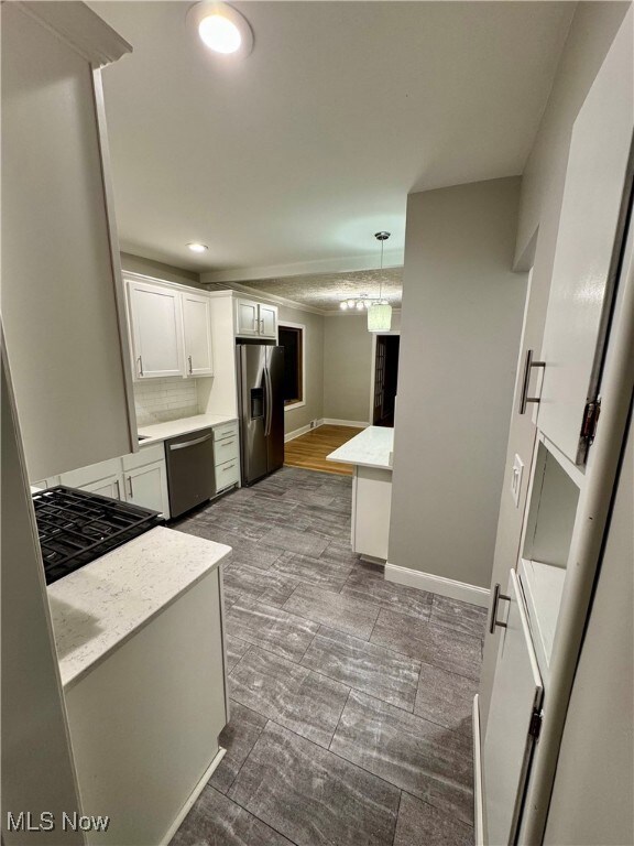 Kitchen with hanging light fixtures, wood-type flooring, white cabinetry, appliances with stainless steel finishes, and decorative backsplash