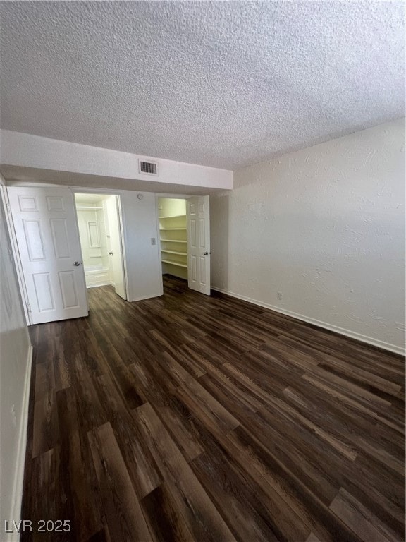 Unfurnished bedroom featuring dark wood-style flooring, a textured ceiling, and a spacious closet