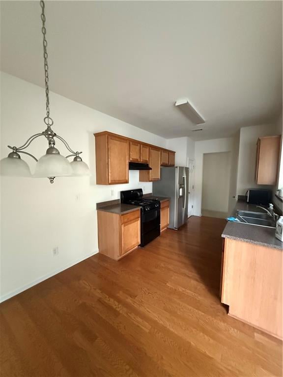 Kitchen with gas range oven, a sink, fridge, dark countertops, and dark wood-style floors