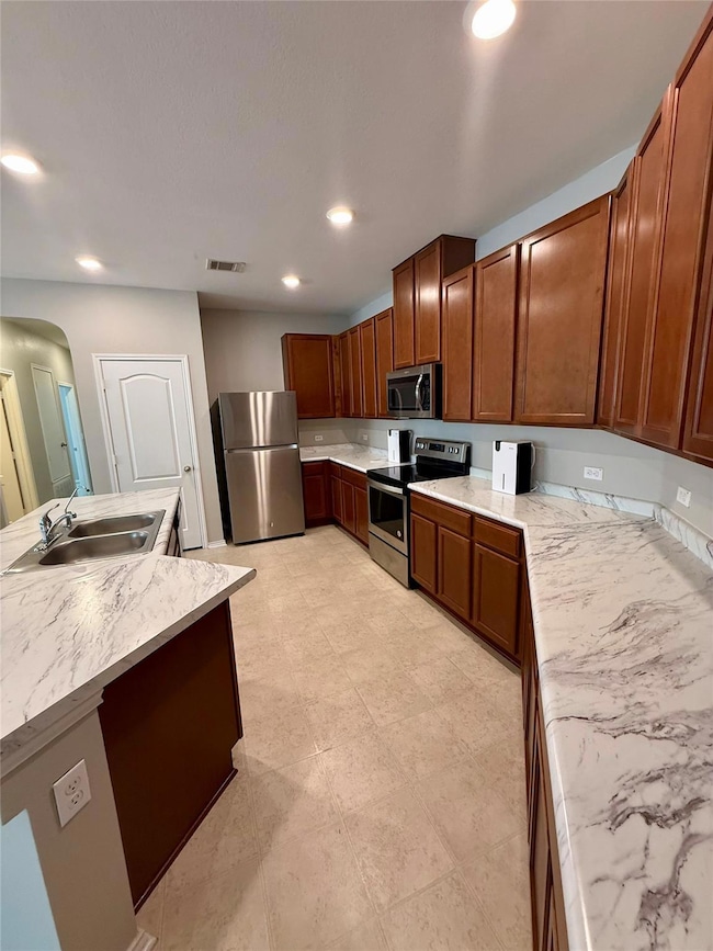 Kitchen with light countertops, appliances with stainless steel finishes, arched walkways, recessed lighting, and an island with sink