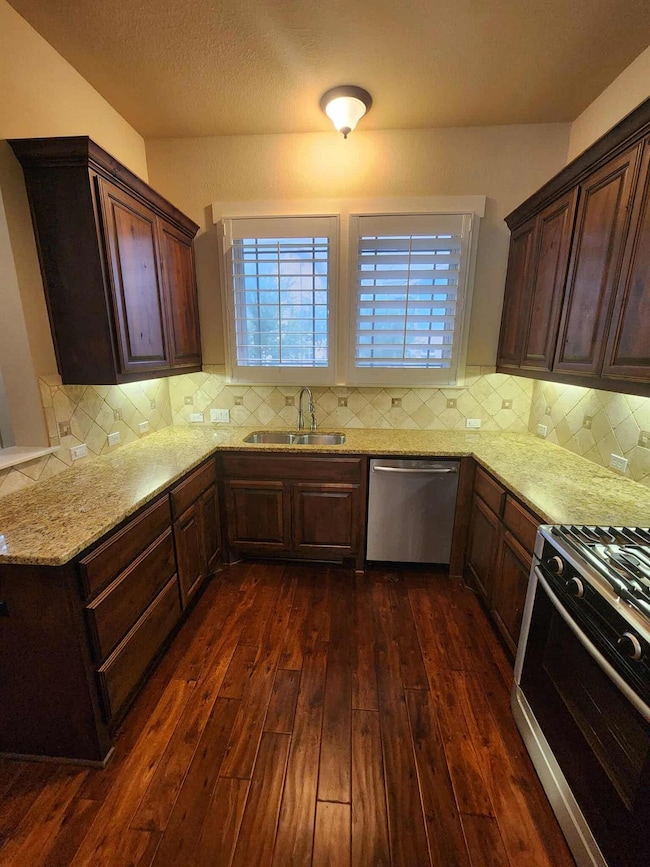 Kitchen with stainless steel appliances, light stone countertops, dark brown cabinets, decorative backsplash, and dark wood-style floors