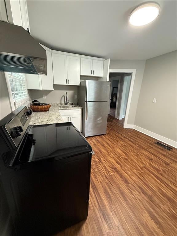 Kitchen featuring electric range oven, white cabinets, freestanding refrigerator, range hood, and light stone countertops