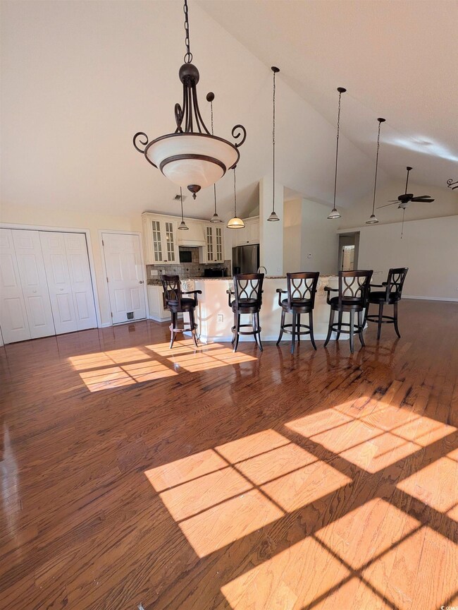 Kitchen with wood finished floors, decorative light fixtures, glass insert cabinets, a kitchen bar, and a ceiling fan