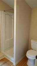 Bathroom with a shower stall, toilet, and tile pa