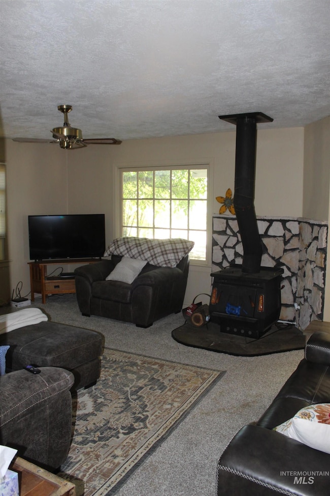 Carpeted living area with a textured ceiling, a wood stove, and a ceiling fan