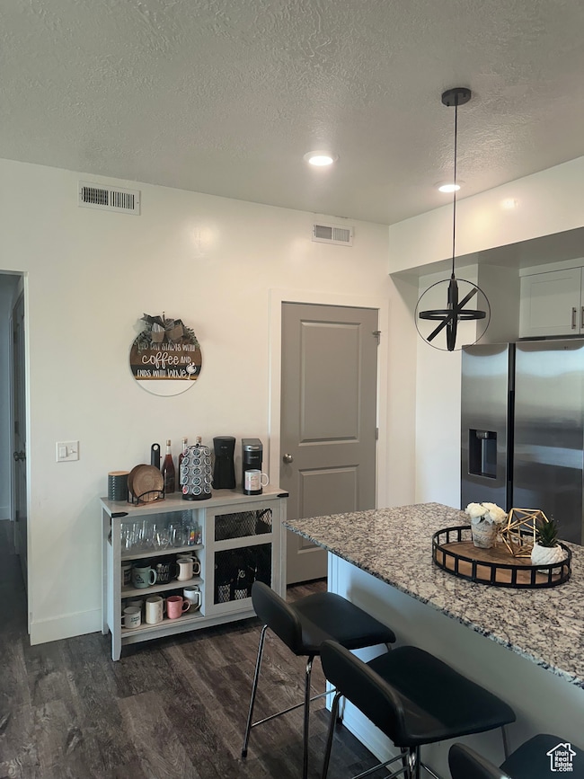 Kitchen featuring a kitchen bar, stainless steel fridge, dark wood-style flooring, a textured ceiling, and light stone countertops