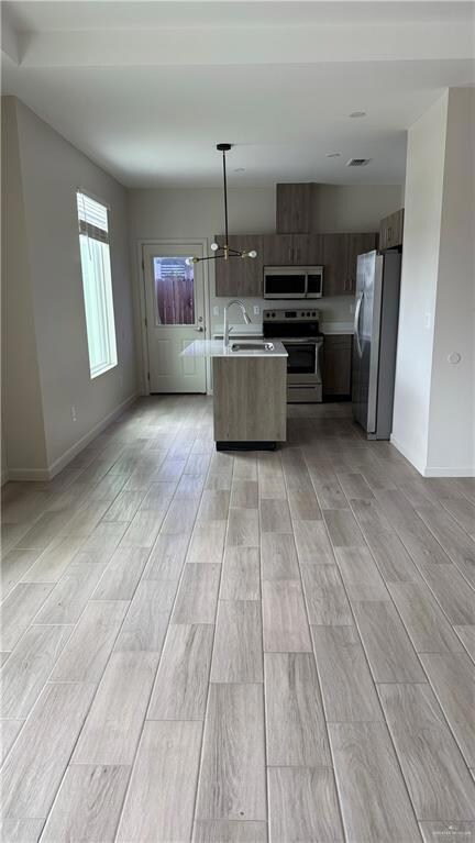 Kitchen with sink, an island with sink, light hardwood / wood-style floors, decorative light fixtures, and appliances with stainless steel finishes
