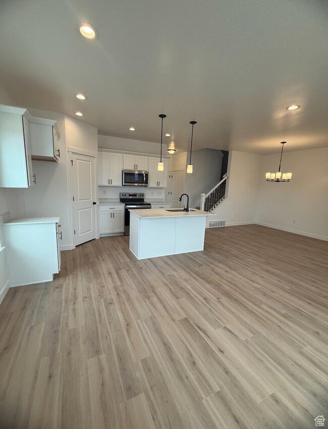 Kitchen featuring white cabinetry, recessed lighting, open floor plan, appliances with stainless steel finishes, and hanging light fixtures