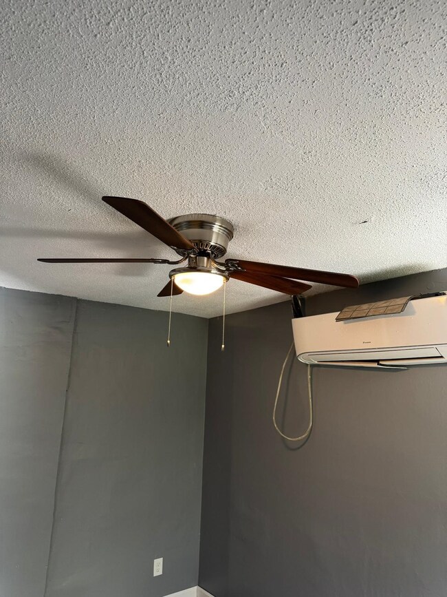 Detailed view of a textured ceiling, an AC wall unit, and ceiling fan
