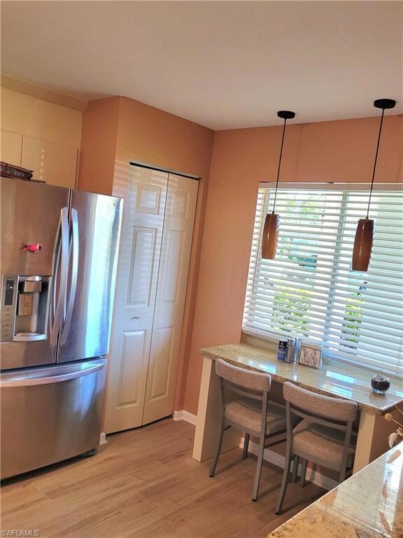 Kitchen featuring stainless steel fridge with ice dispenser, hanging light fixtures, and light wood finished floors
