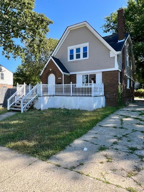 View of front of home featuring brick siding, a chimney, a wooden deck, and a front yard