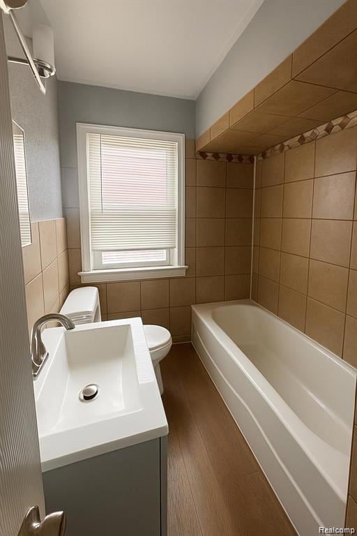 Bathroom featuring tile walls, dark wood-style flooring, vanity, and bathing tub / shower combination