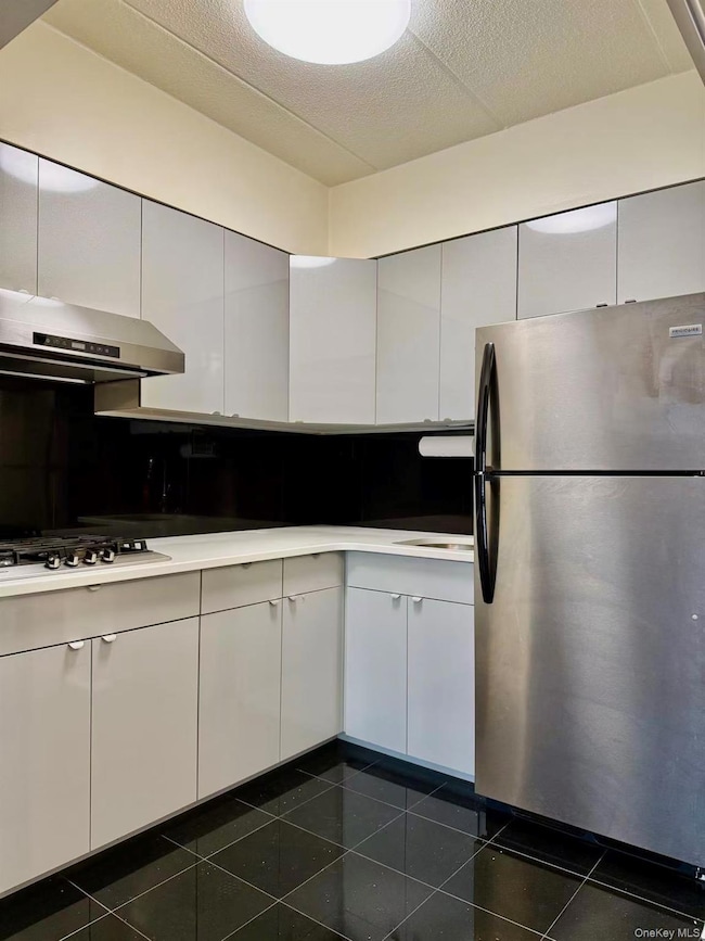 Kitchen featuring appliances with stainless steel finishes, white cabinetry, under cabinet range hood, light countertops, and a textured ceiling
