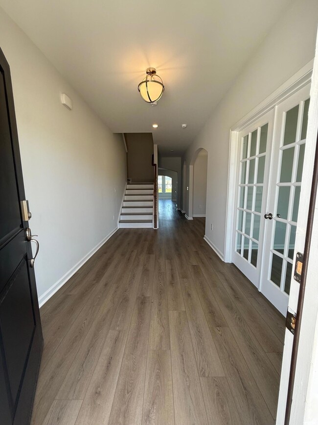 Hallway featuring arched walkways, wood finished floors, stairs, baseboards, and french doors