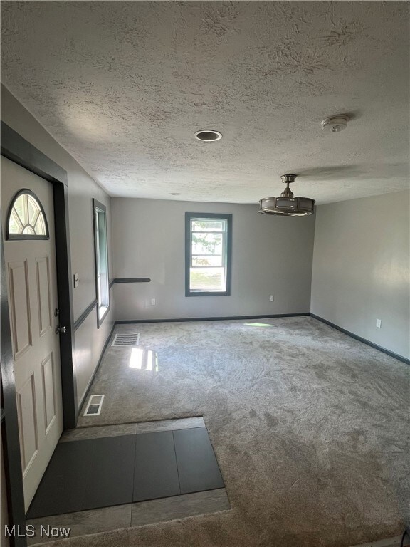 Carpeted entryway featuring a textured ceiling and baseboards