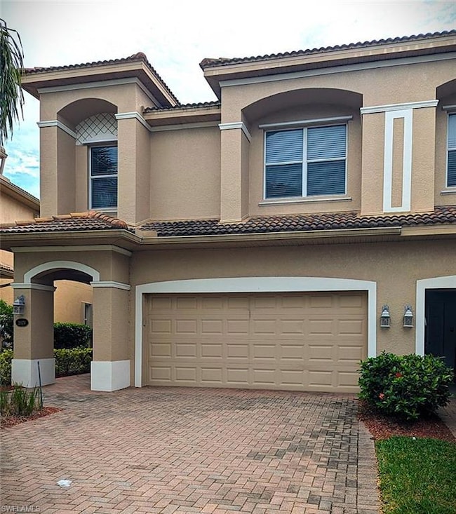 Mediterranean / spanish-style house featuring a tile roof, decorative driveway, an attached garage, and stucco siding
