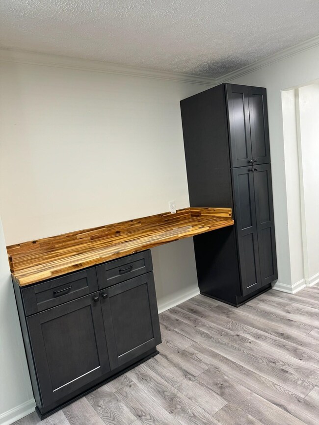 Kitchen featuring wood counters, light wood-style flooring, ornamental molding, a textured ceiling, and baseboards