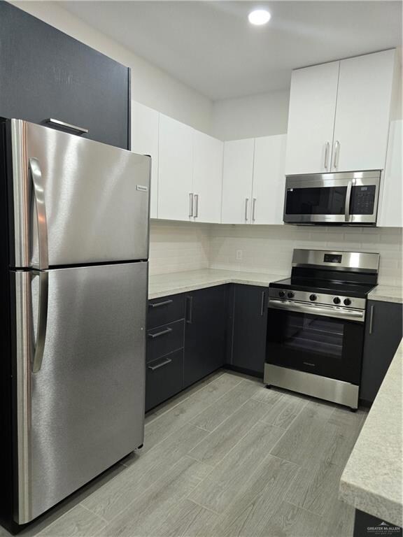 Kitchen featuring backsplash, stove, fridge, white cabinets, and light wood-type flooring