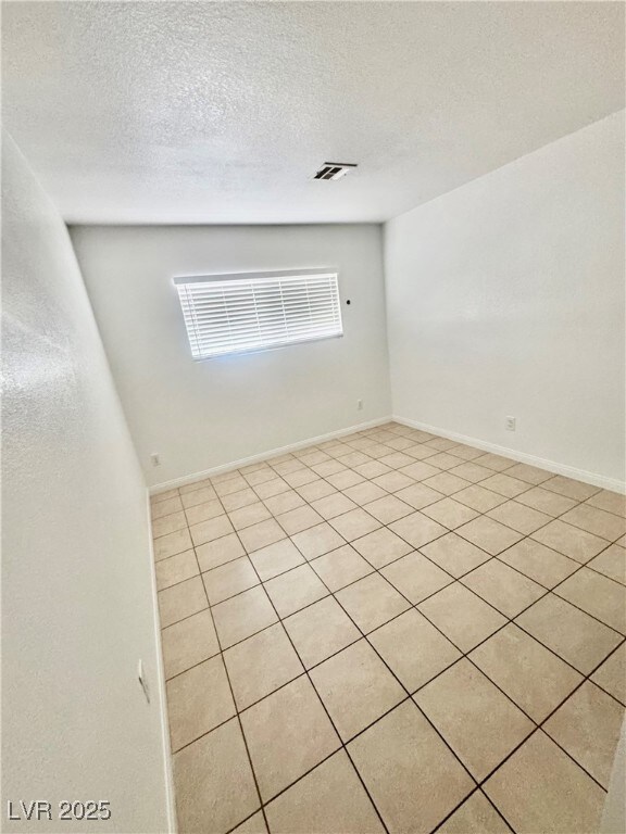 Tiled empty room with a textured ceiling and baseboards