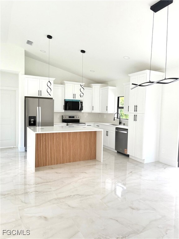 Kitchen with a center island, white cabinetry, light marble finish floors, lofted ceiling, and pendant lighting