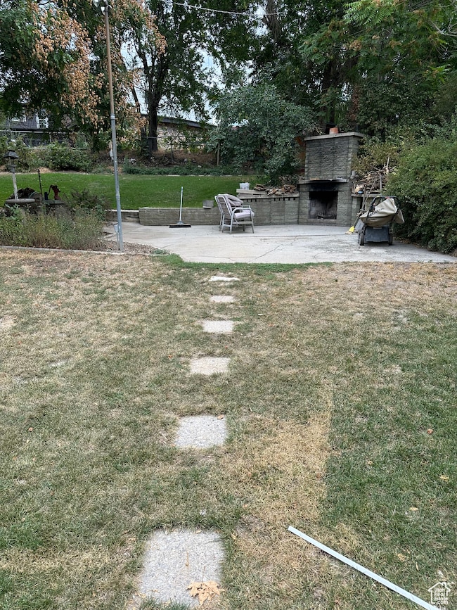 View of grassy yard featuring a patio and an outdoor fireplace