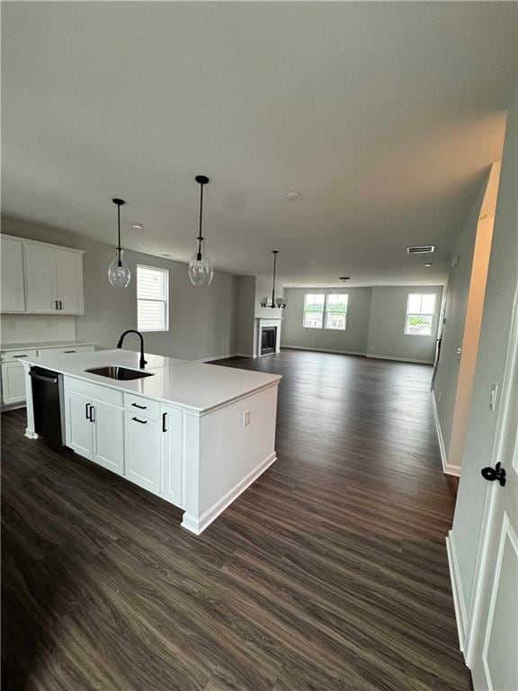 Kitchen featuring a sink, dishwasher, open floor plan, a kitchen island with sink, and white cabinets
