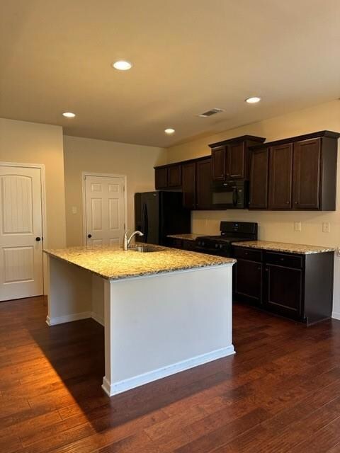 Kitchen featuring fridge, range, dark brown cabinetry, a center island with sink, and dark wood finished floors