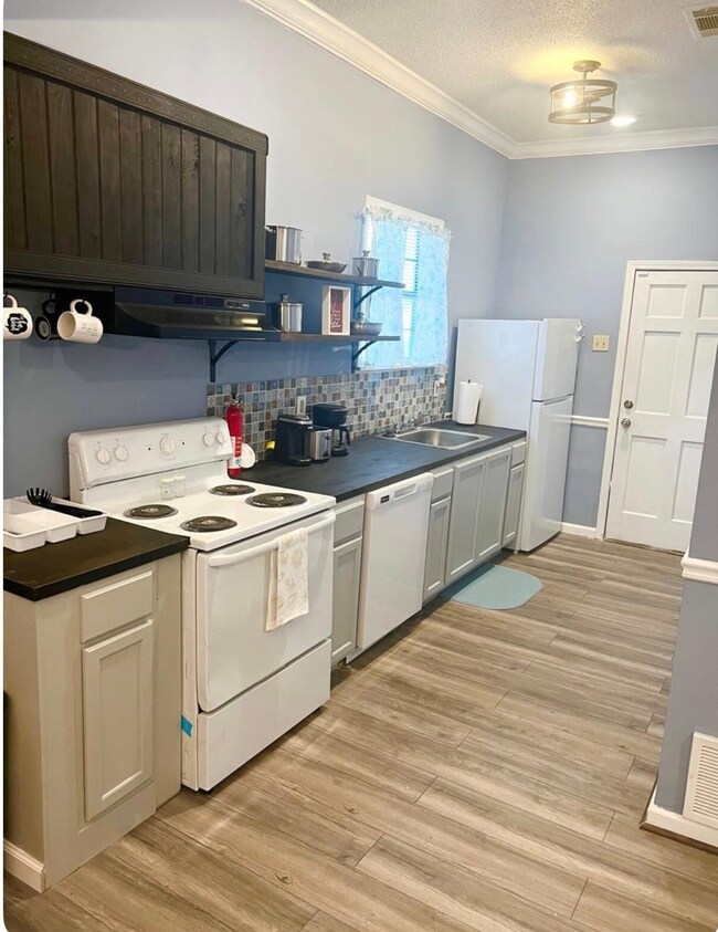 Kitchen featuring white appliances, ornamental molding, decorative backsplash, under cabinet range hood, and light wood-style floors