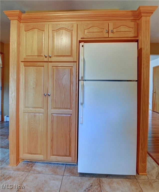 Kitchen with freestanding refrigerator, light brown cabinetry, a baseboard heating unit, and light tile patterned floors